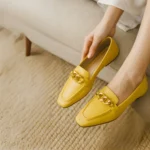 Sleek women’s loafers in a bold yellow finish, accented with a polished gold chain detail across the vamp for a modern twist on a classic silhouette. Lightweight and easy to slip on