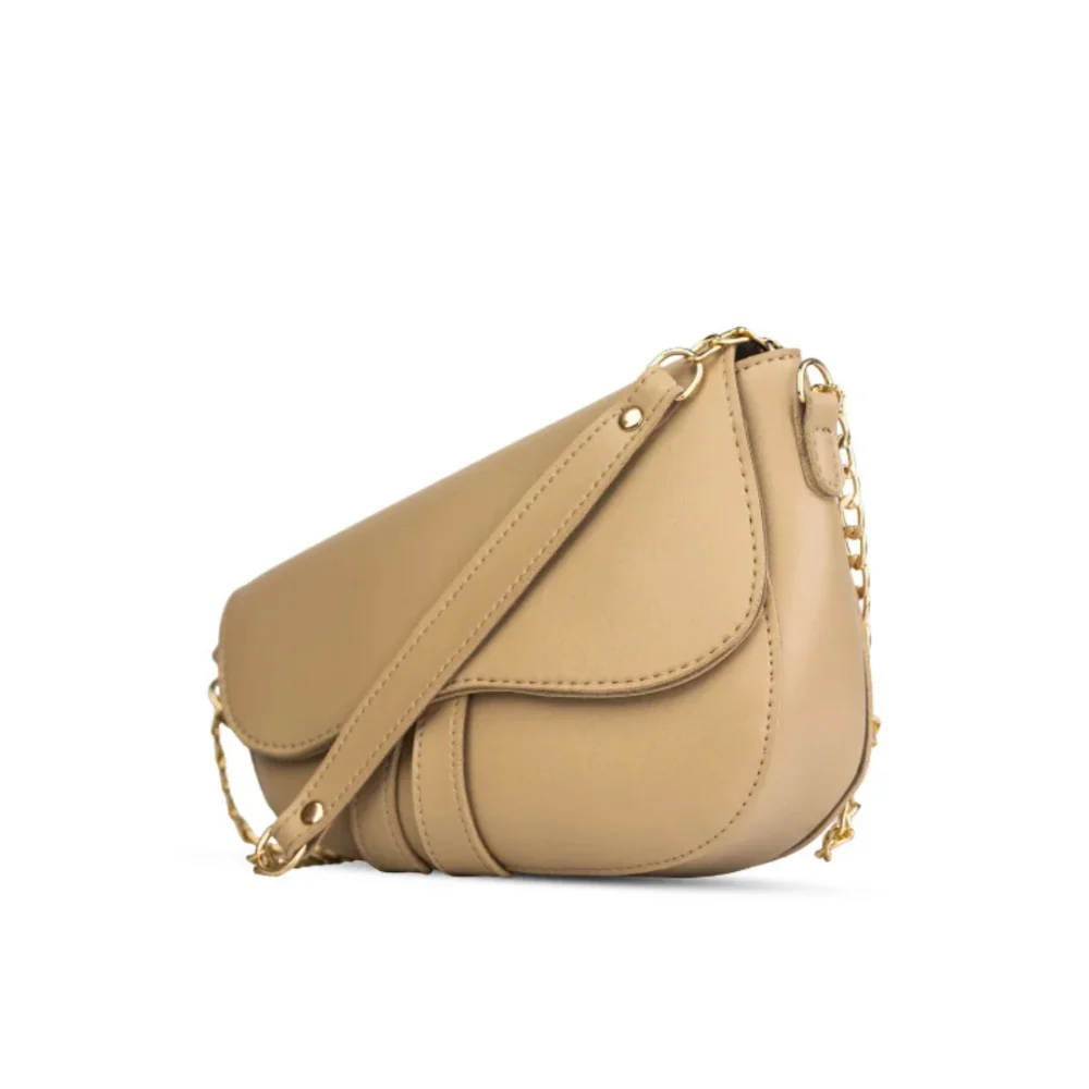 Nude beige crescent-shaped saddle bag with gold chain strap and smooth vegan leather finish.