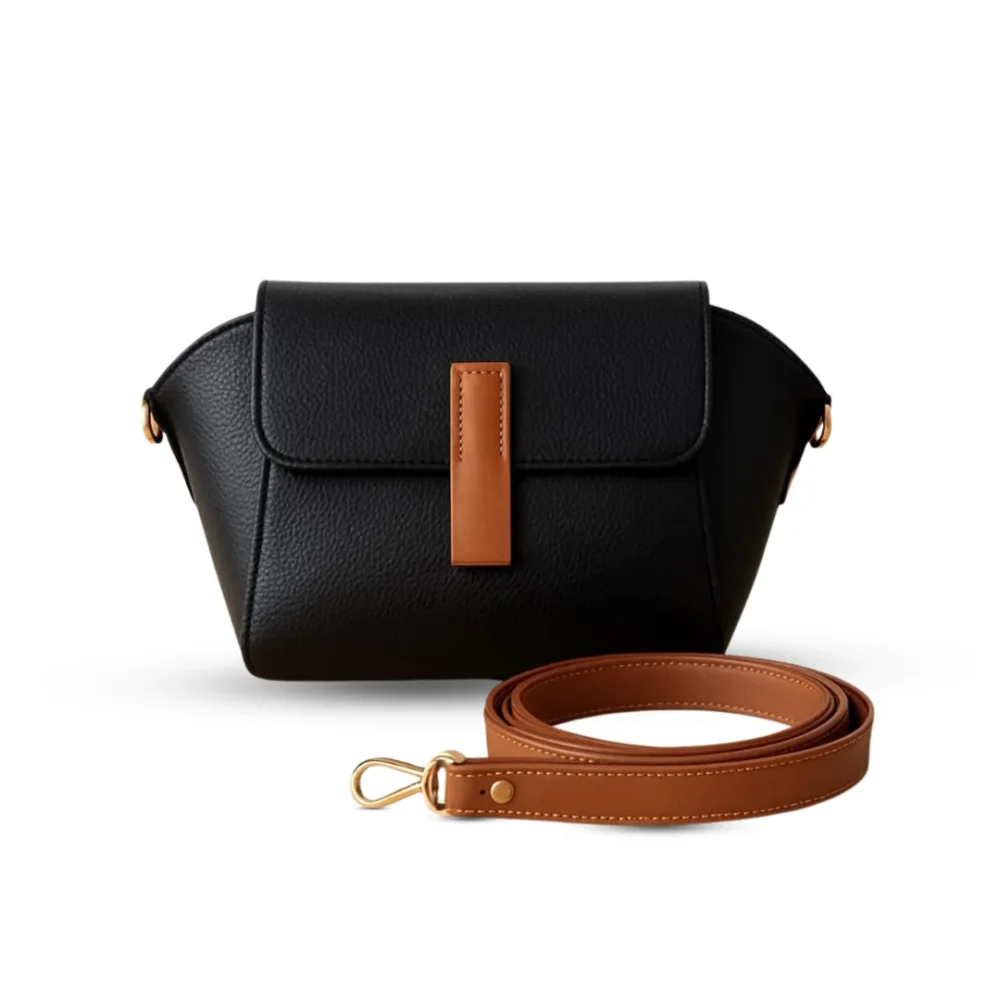 Black pebbled vegan leather crossbody bag with a caramel brown magnetic flap detail and adjustable shoulder strap.