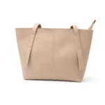 Front view of a soft nude beige minimalist tote bag with a central seam detail and long shoulder straps.