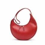 Side view of a smooth red crescent hobo bag with gold zippers and an integrated shoulder strap