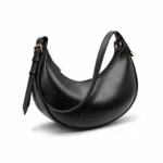 Side view of a smooth black crescent hobo bag with gold zippers and an integrated shoulder strap.
